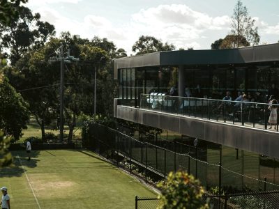 Beautiful outdoor tennis court next to a modern clubhouse under a clear blue sky.