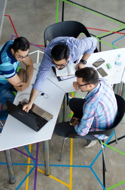 Three men collaborating over a laptop in a modern, geometric-themed office space.