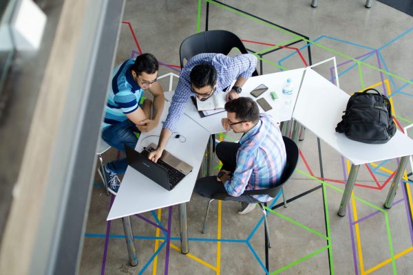 Three men collaborating over a laptop in a modern, geometric-themed office space.