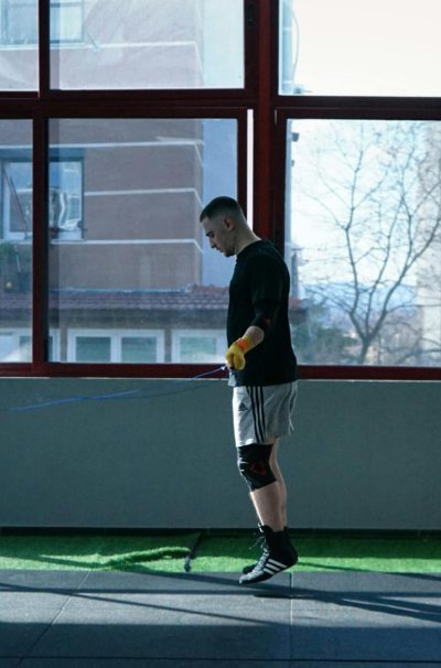 Young man exercising with a skipping rope in an urban gym with large windows and city view.