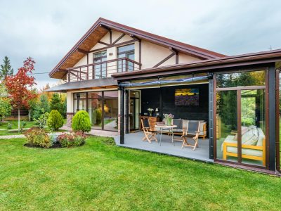 Residential cottage with balcony and opened veranda opening view on lawn and trees growing in backyard